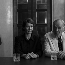A woman and an older man sit next to each other looking forward - the photo is in black and white