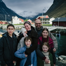 A happy family photo of 7 - standing outside with mountains in the backgroound