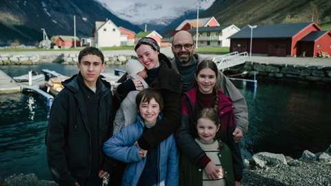 A happy family photo of 7 - standing outside with mountains in the backgroound