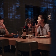 A family of three are sat at the dinner table smiling.