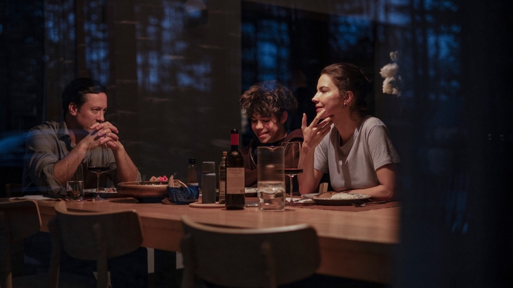 A family of three are sat at the dinner table smiling.