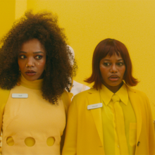 Three people standing in a row looking slightly confused all dressed in yellow against a yellow backdrop