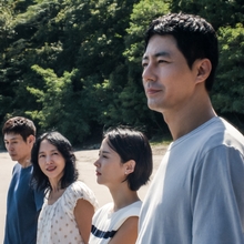 A group of four people stand on the shoreline looking out to the water