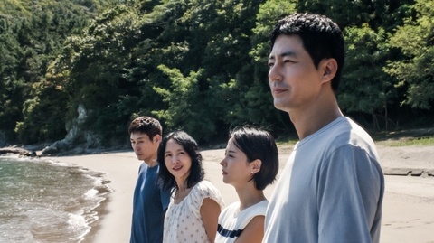 A group of four people stand on the shoreline looking out to the water