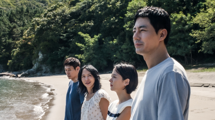 A group of four people stand on the shoreline looking out to the water
