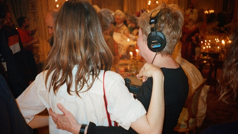 Two people standing with their arms around one another, one of them wearing headphones