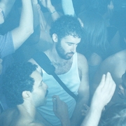 A crowded club dance floor with one person in a white vest looking down with their eyes closed