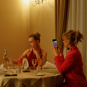 A still of three people sitting at a dinner table all on their phones.