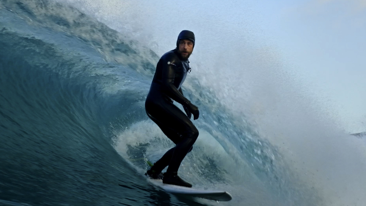Surfer in a black wetsuit riding a large, curling wave under a clear sky.