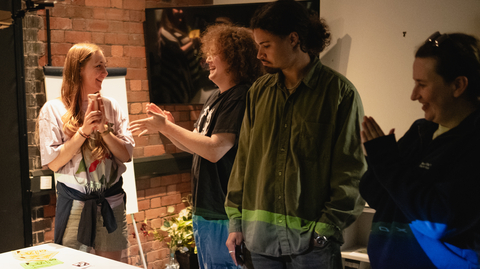 A diverse group chats and laughs around a table covered with colorful sticky notes, creating a warm, collaborative workshop atmosphere.