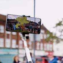 Smartphone on a selfie stick displays an augmented-reality view of a historic street scene.