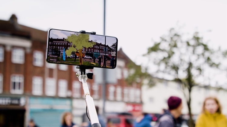 Smartphone on a selfie stick displays an augmented-reality view of a historic street scene.
