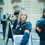 Police investigators in a city street, with a blonde woman facing the camera and surveying equipment in the foreground.