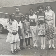 A black and white photograph of a group of children standing together smiling, posssibly from some time in the early 1970s
