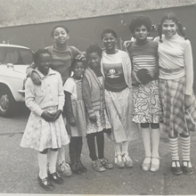 A black and white photograph of a group of children standing together smiling, posssibly from some time in the early 1970s