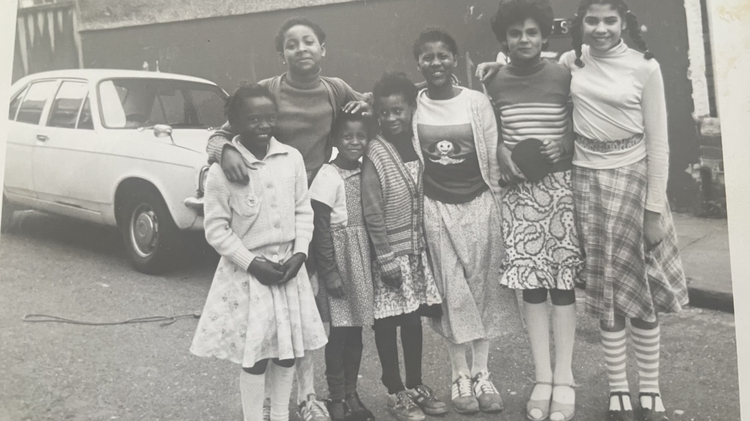 A black and white photograph of a group of children standing together smiling, posssibly from some time in the early 1970s