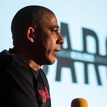 Head shot of a man standing in front of a cinema screen holding a microphone - the word CARGO is on the screen.