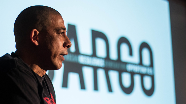 Head shot of a man standing in front of a cinema screen holding a microphone - the word CARGO is on the screen.