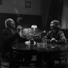 A still of a father and a daughter sitting at a table smoking, drinking and smiling.