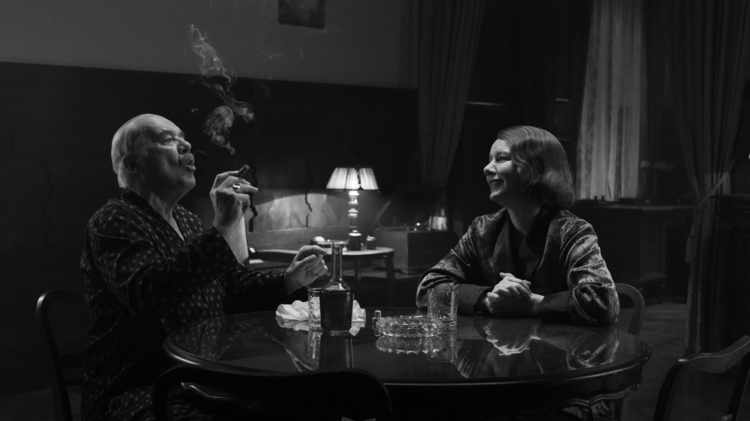 A still of a father and a daughter sitting at a table smoking, drinking and smiling.