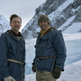 Two men in winter clothing stand on a snowy mountain, smiling with climbing ropes and gear.