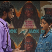 A man and a woman looking at each other standing in front of a wall of posters.