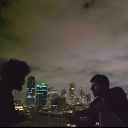 A still of two men talking on a rooftop at night.