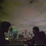 A still of two men talking on a rooftop at night.