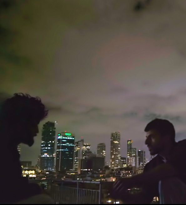 A still of two men talking on a rooftop at night.