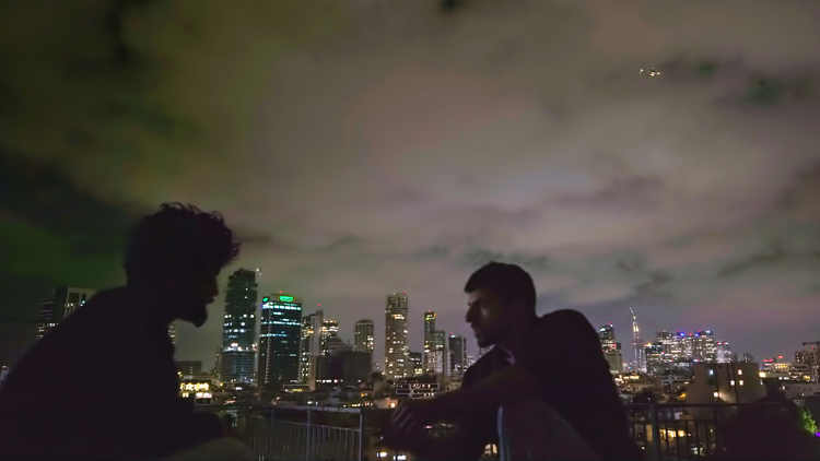 A still of two men talking on a rooftop at night.